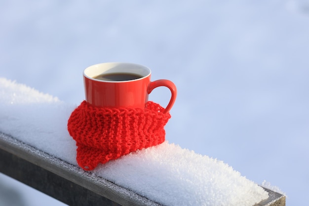 Una tazza di tè caldo in una tazza rossa e una sciarpa lavorata a maglia sullo sfondo della natura innevata Cartolina invernale Messa a fuoco selettiva