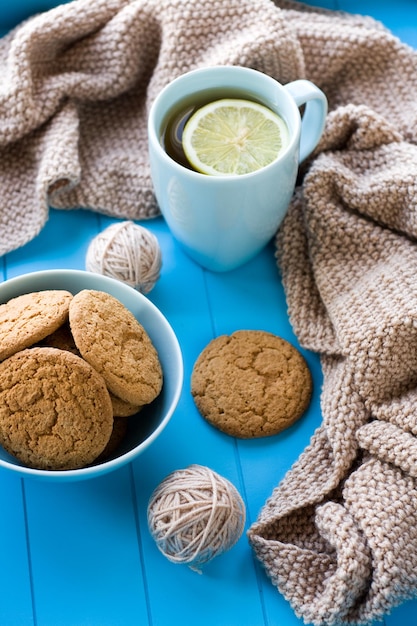 Una tazza di tè con la coperta lavorata a maglia beige dei biscotti al limone si trova sul vassoio blu