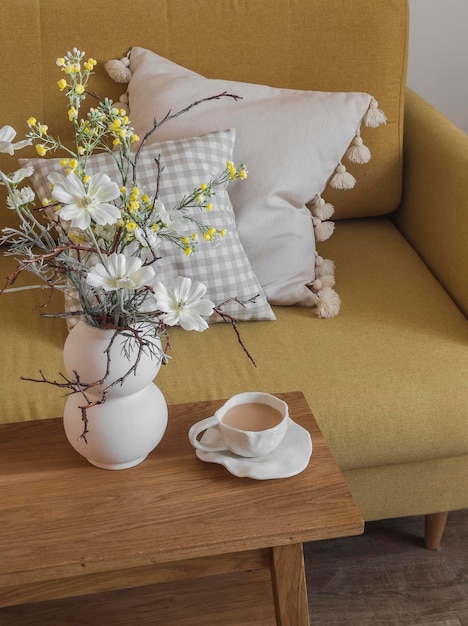 Una tazza di tè con latte un vaso di fiori su un tavolo di legno accanto a una poltrona gialla