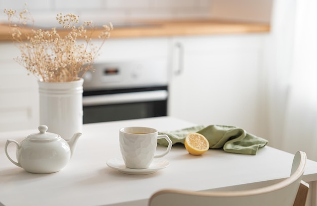 Una tazza di tè con limone e una teiera su un tavolo bianco con un bouquet asciutto