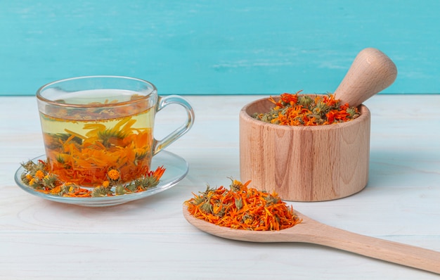 Una tazza di tè di calendula su un tavolo di legno, un mortaio con fiori di calendula