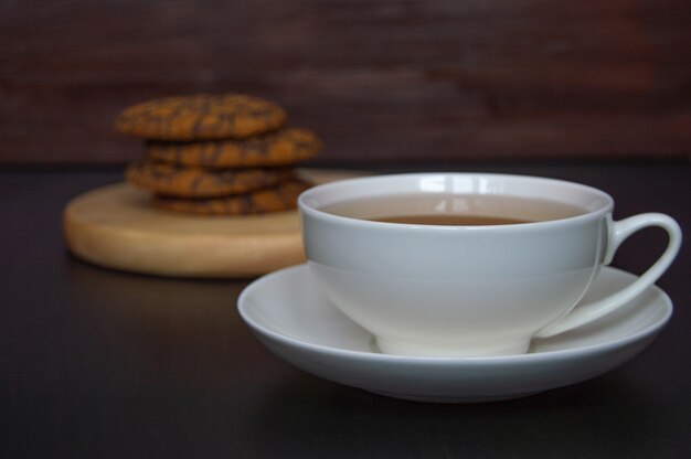 una tazza di tè e biscotti di farina d'avena su un supporto di legno su uno sfondo scuro