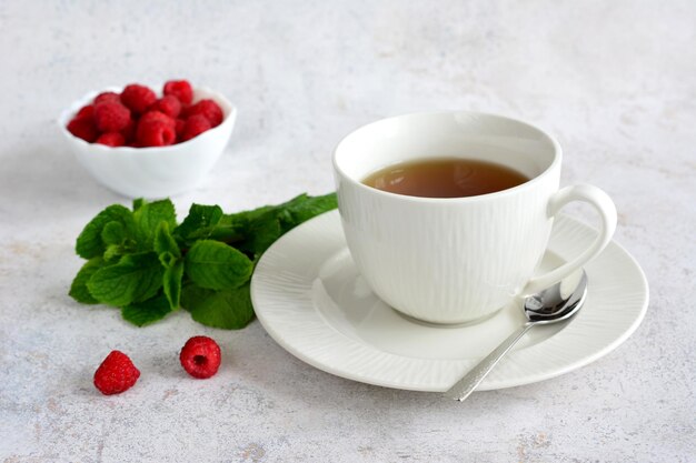 una tazza di tè e un cucchiaio su un piatto con menta e lamponi