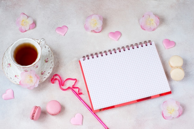 una tazza di tè, fiori, amaretti, un quaderno con fogli vuoti e una penna