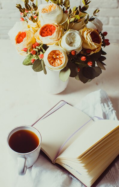 Una tazza di tè nero, taccuino e bellissimi fiori sul tavolo. Ispirazione mattutina per la pianificazione della giornata
