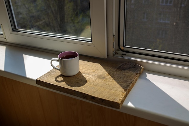 Una tazza di tè su un vassoio di legno è in piedi vicino alla finestra