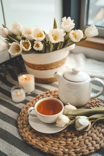 Una tazza di tè sullo sfondo di un cesto con tulipani in un'accogliente natura morta primaverile interna