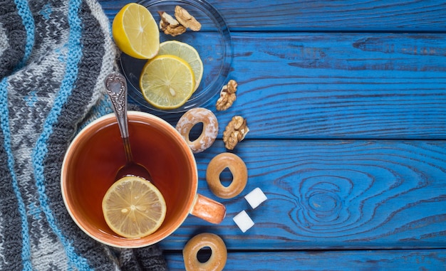 Una tazza di tè, una sciarpa lavorata a maglia e bagel sullo sfondo di un tavolo di legno blu