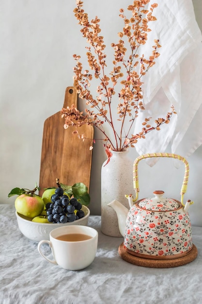 Una tazza di tè una teiera una ciotola di frutta su un tavolo luminoso con fiori secchi in un vaso Umore autunnale a casa ancora in vita