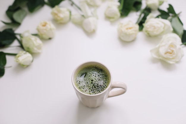 Una tazza di tè verde con rose bianche su sfondo bianco. Flatlay, vista dall'alto, copia spazio.