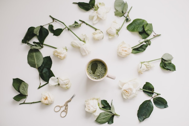 Una tazza di tè verde con rose bianche su superficie bianca