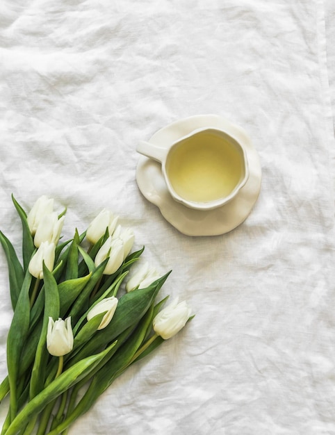 Una tazza di tè verde e un bouquet di tulipani bianchi sulle lenzuola bianche del letto