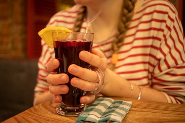 una tazza di vetro con un delizioso vin brulé aromatico fatto in casa tiene la mano della ragazza sfocata e si crogiola su di essa. messa a fuoco morbida, primo piano.