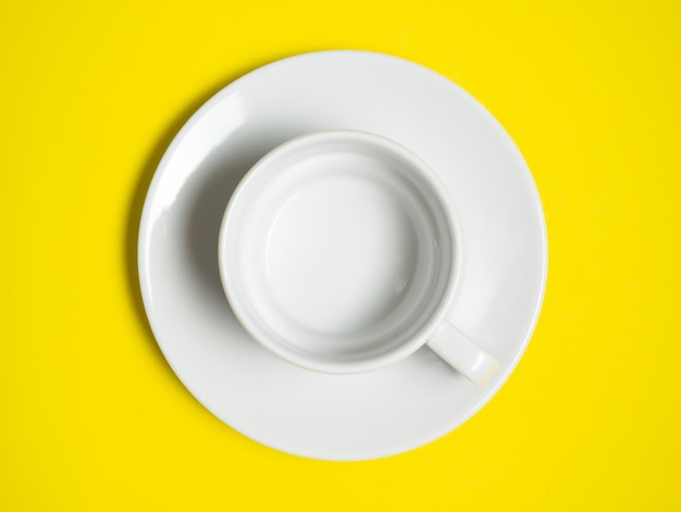 Una tazza e un piattino bianchi vuoti su una superficie gialla