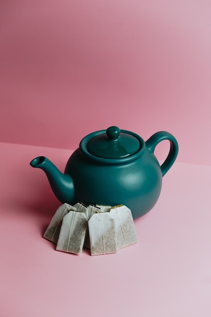 Una teiera blu minimalista e buste per tè veloci su uno sfondo rosa pastello
