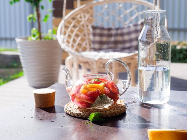 Una teiera di vetro con frutta e bacche di foglie di menta sul tavolo esterno Tè alla frutta estiva