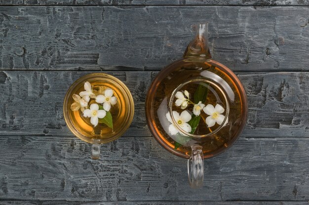 Una teiera di vetro e una ciotola con fiori di tiglio su un tavolo di legno nero. Una bevanda tonificante che fa bene alla salute.