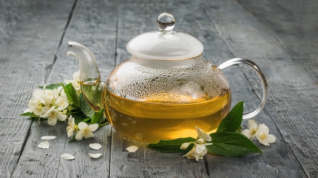 Una teiera di vetro piena di tè medicinale con fiori di gelsomino. Una bevanda tonificante che fa bene alla salute.