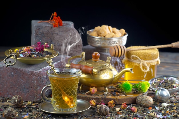 Una teiera e una tazza di tè siedono su un tavolo con altri oggetti tra cui una ciotola di miele e una ciotola di miele.