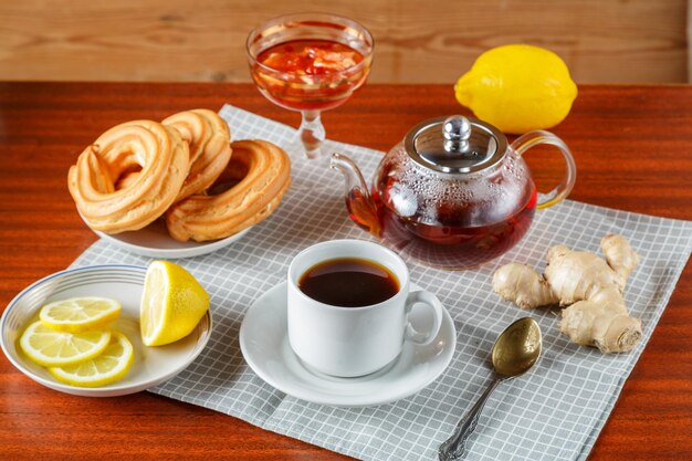 Una teiera e una tazza e un piattino di tè aromatico forte sul tavolo su un tovagliolo accanto a ciambelle e marmellata di zenzero e limone.