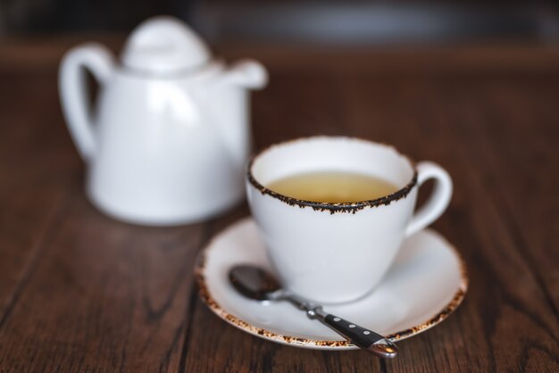una teiera in ceramica bianca e una tazza di tè aromatico corroborante su un tavolo di legno marrone