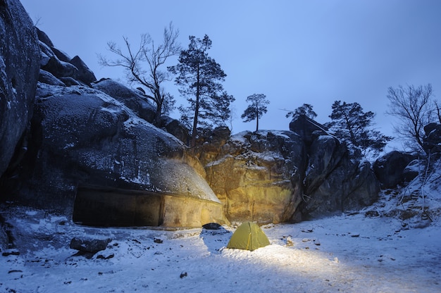 Una tenda verde in piedi sulla neve accanto alla scogliera rocciosa