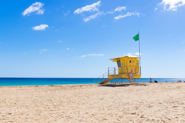 Una torretta gialla del bagnino su una spiaggia con una bandiera verde nei precedenti.