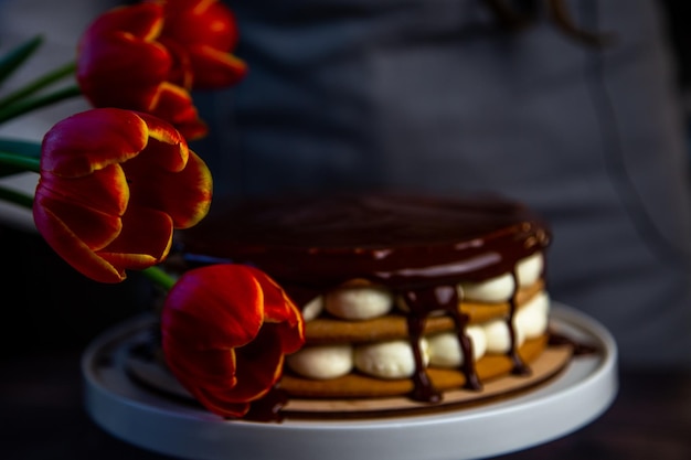 Una torta con torte al miele e crema bianca si trova su un supporto bianco e viene versata sopra il cioccolato ...