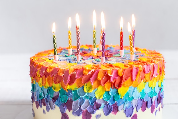 Una torta di compleanno multicolore decorata con candele accese. Concetto di auguri di buon compleanno.