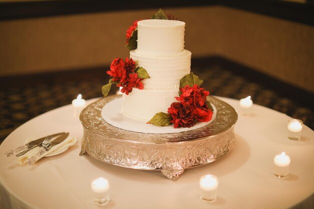 Una torta nuziale bianca con fiori rossi su un tavolo d'argento.