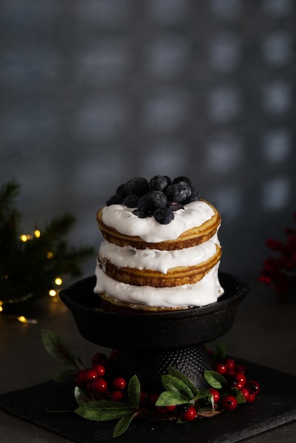 Una torta pancake decorata a festa con panna e mirtilli si trova su un supporto di pietra nera