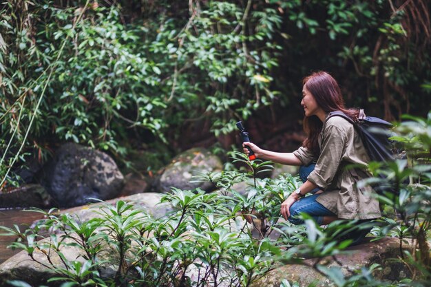 Una turista con lo zaino che riprende il video della cascata nella foresta con una action camera