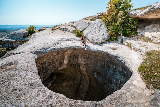 Una turista donna siede sul bordo di un enorme buco nella grotta. Pittoresco fenomeno naturale