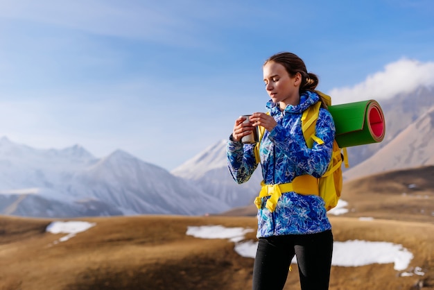 Una turista felice beve il tè su uno sfondo di bellissime montagne innevate