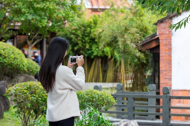 Una turista usa una fotocamera digitale per scattare una foto nel giardino cinese