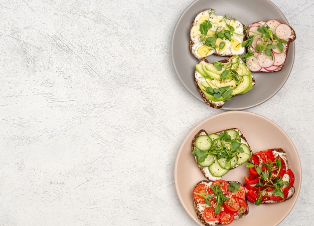 Una varietà di mini panini con crema di formaggio e verdure su piatti su una superficie leggera