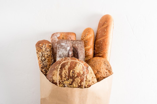 Una varietà di pane fresco e delizioso in un sacchetto di carta con manici su sfondo bianco il concetto di shopping senza sprechi