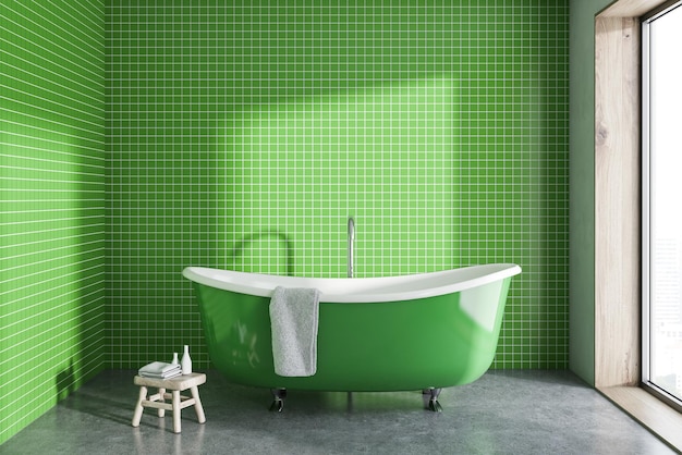 Una vasca da bagno verde con un asciugamano appeso su di essa in piedi su un pavimento di cemento di un bagno minimalista.