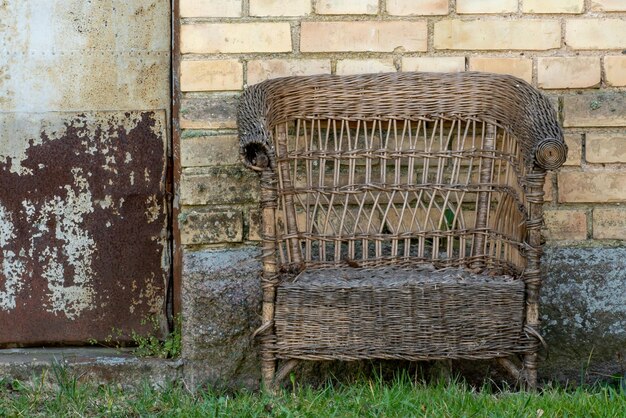 Una vecchia sedia di vimini si trova all'esterno vicino a una casa di mattoni Sedile libero sulla poltrona Un luogo accogliente per rilassarsi nella natura