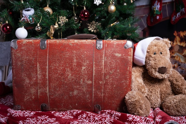 Una vecchia valigia da viaggio rossa si trova accanto a un orso giocattolo e un albero di Natale decorato