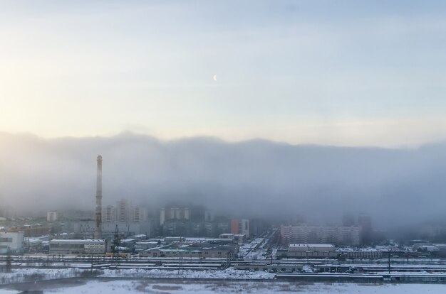 Una veduta della città avvolta dallo smog mattutino, nel cielo la luna.