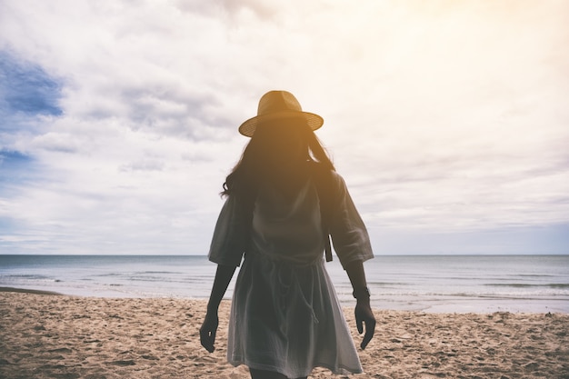 Una viaggiatrice con cappello e zaino che cammina sulla spiaggia in riva al mare