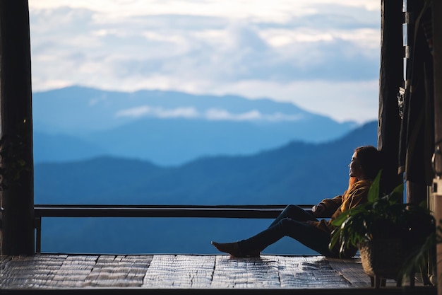 Una viaggiatrice seduta e guardando una bellissima vista sulle montagne e sulla natura prima del tramonto
