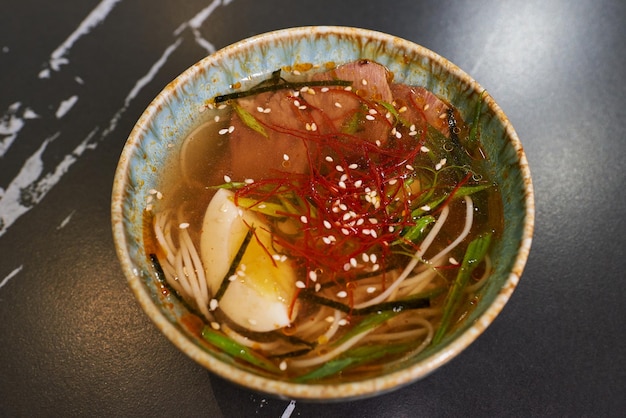 Una vista dall'alto della tradizionale zuppa giapponese Ramen con uova e carne di maiale in una ciotola di ceramica blu su un tavolo di pietra nera