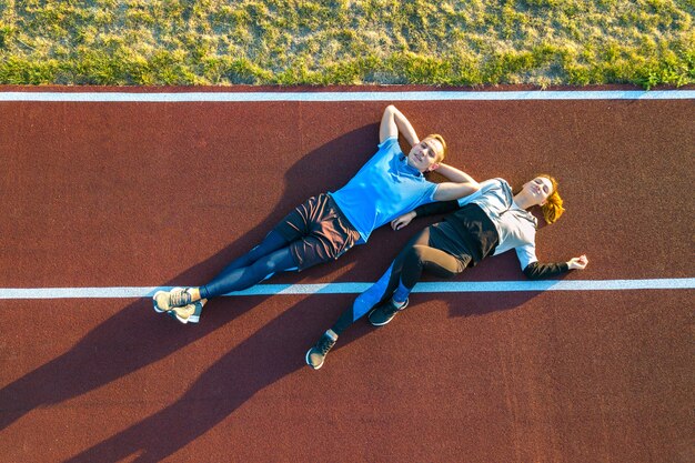 Una vista dall'alto in basso di due giovani sportivi e sportivi che pongono sulla pista corrente di gomma rossa di un campo dello stadio che riposa dopo la maratona pareggiante in estate.