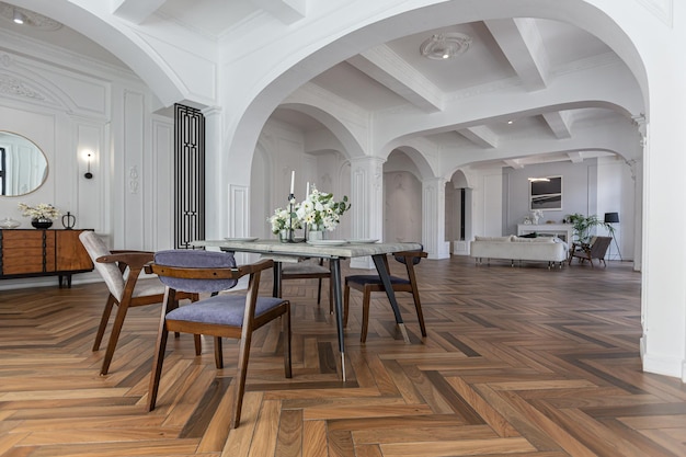 una vista di un tavolo da pranzo impostato in un elegante interno luminoso costoso di un enorme salotto in un palazzo storico con archi ad arco, colonne e pareti bianche decorate con ornamenti e stucco