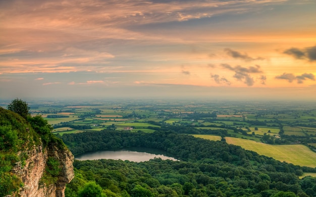 una vista di un tramonto da una scogliera con un lago in lontananza