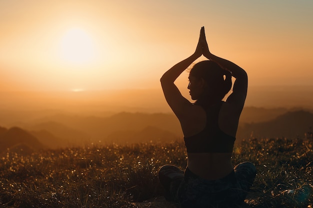 Una vista posteriore della silhouette di una donna che pratica lo yoga in natura. Posizione del loto con le mani sopra la testa