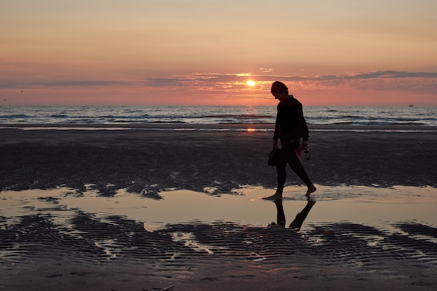 Una vista posteriore di una signora che cammina sulla spiaggia godendosi il tramonto panoramico