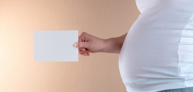 Una vista ravvicinata del ventre di una donna incinta in una maglietta bianca.